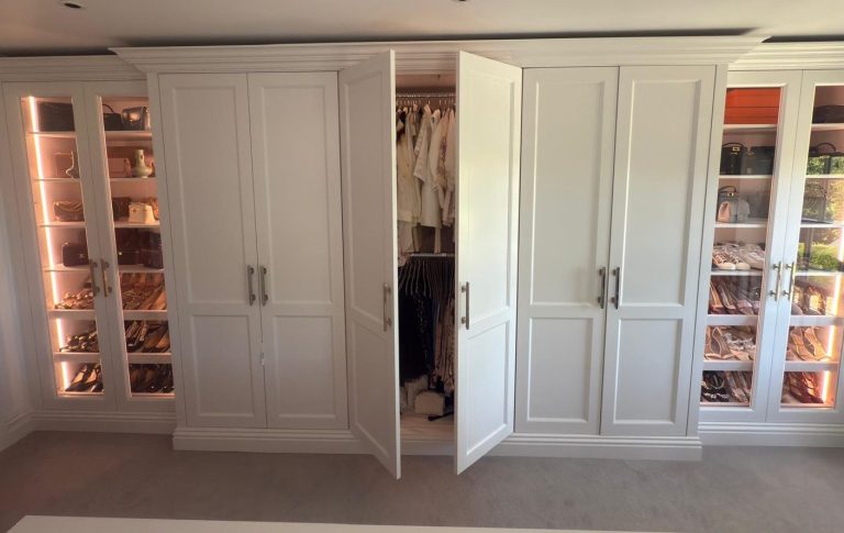 Modern white wardrobe with open doors revealing clothes inside, flanked by glass cabinets.
