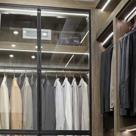 A modern wardrobe featuring neatly arranged shirts and suits behind glass doors.