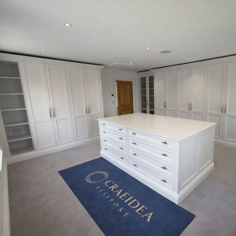Bright walk-in wardrobe featuring white cabinetry and a central island with drawers.