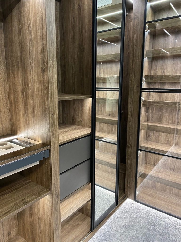 Wooden wardrobe interior with shelves, drawers, and a full-length mirror.