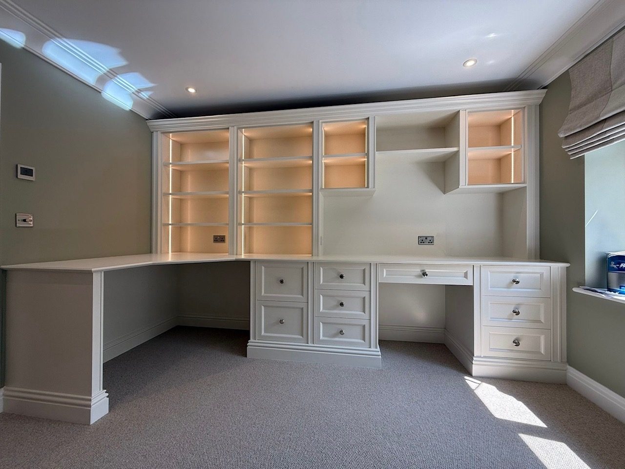 Light green room with a built-in desk and shelving unit, empty and well-lit.