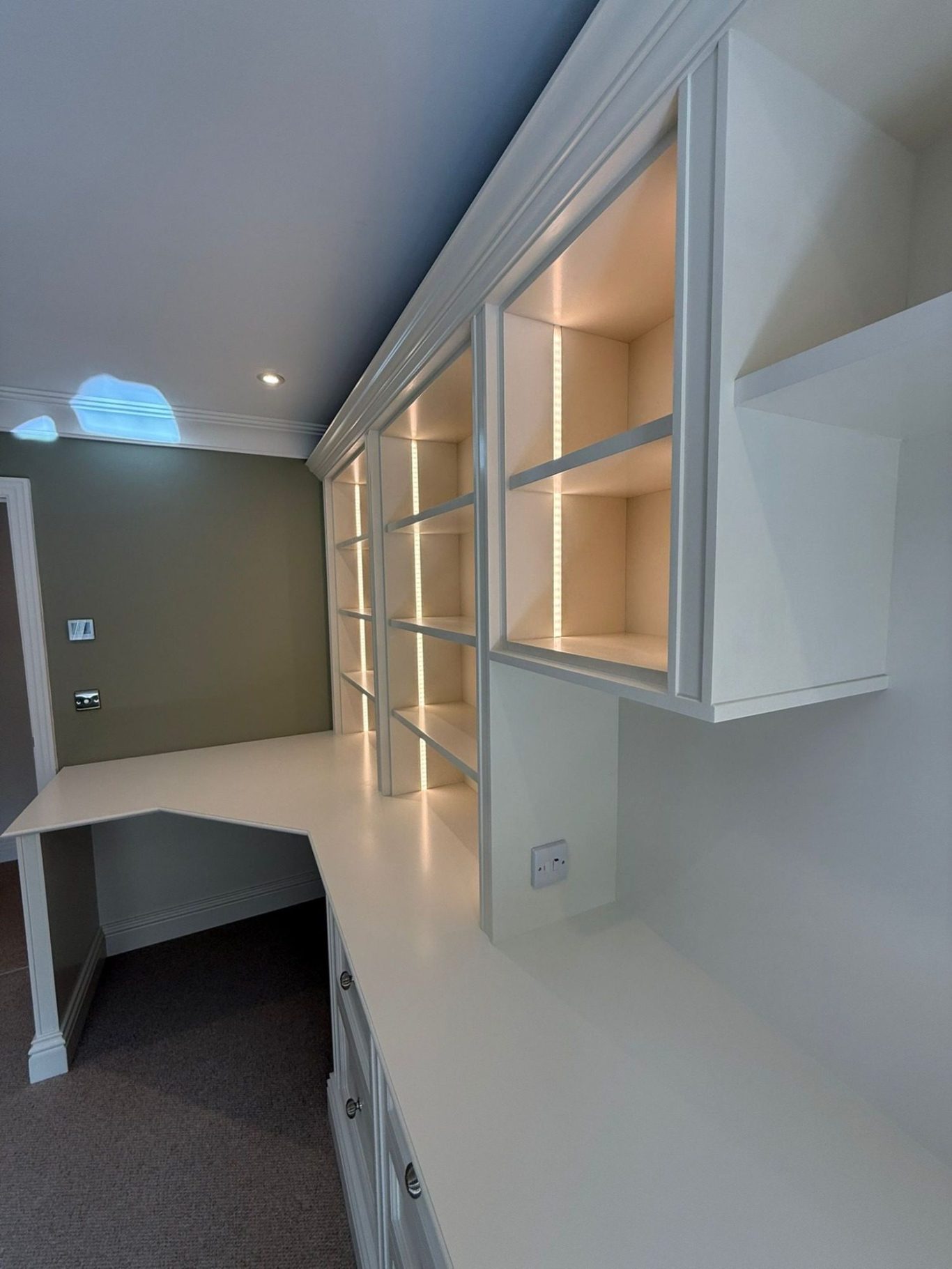 A modern white countertop with built-in shelves and soft lighting against a grey wall.