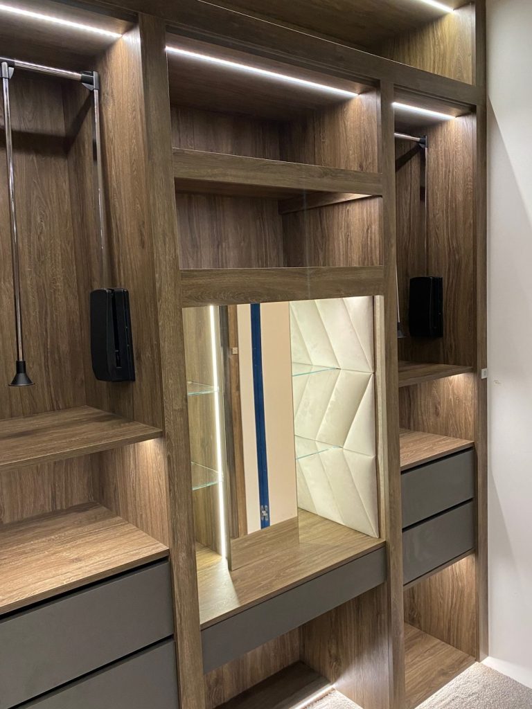 Modern wooden wardrobe with lighting, shelves, and a central mirror.